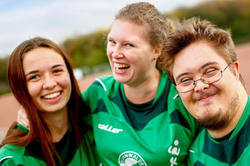 Drei Jugendliche in Sporttrikot umarmen sich.