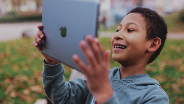Ein Junge schaut auf ein Tablet und lächelt.