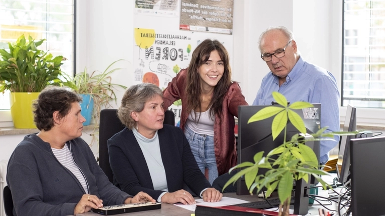 Zwei Frauen mit Braille-Tastatur sitzen vor einem Bildschirm, eine weitere Frau und ein Mann schauen auf den Bildschirm.