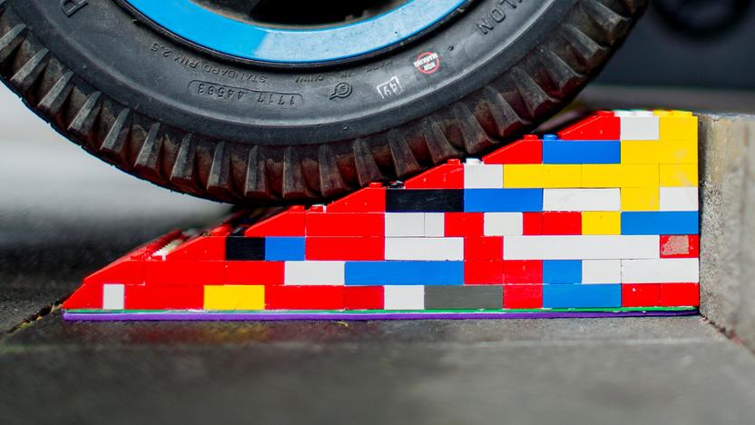 Eine bunte Legorampe liegt vor einer Stufe. Im Anschnitt ist ein Rollstuhl- oder Kinderwagen-Reifen zu sehen, der gerade über die Rampe rollt.