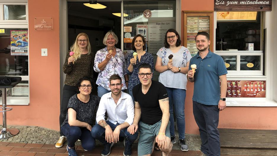 Eine Gruppe von Menschen steht lachend vor dem Eiscafé Dolomiti.