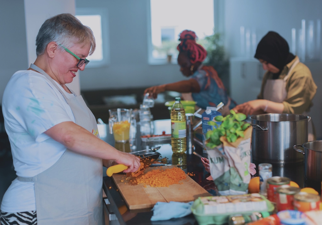 Drei Frauen aus verschiedenen Ländern bereiten gemeinsam Gerichte aus verschiedenen Kulturen zu.