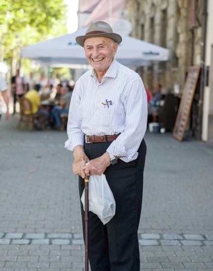 Ein älterer Mann mit einem Gehstock in der Hand steht in der Stadt und lächelt