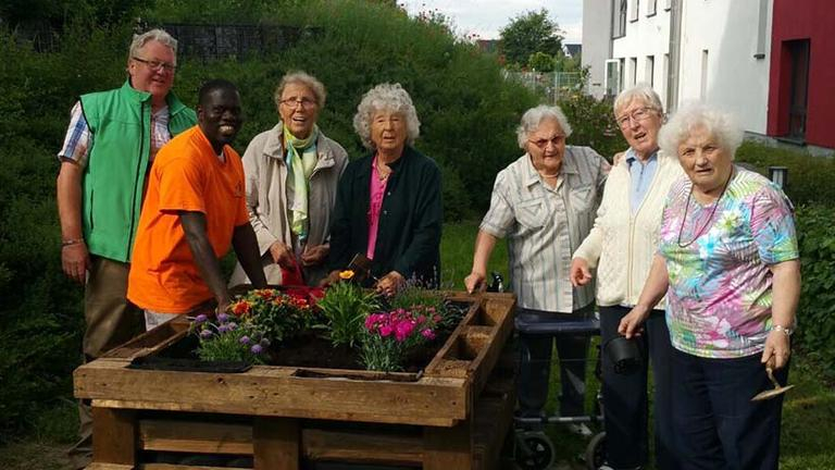 Senioren und Seniorinnen stehen neben einem Hochbeet und schauen in die Kamera.