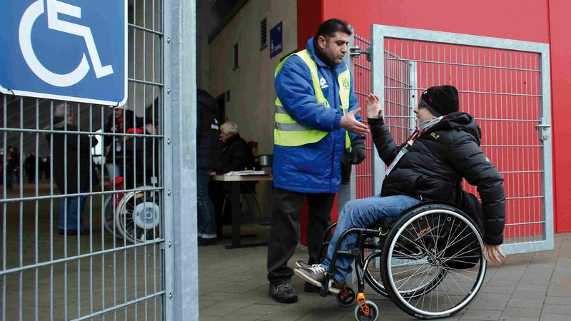 Rollifahrer begrüßt einen Ordner am Eingang