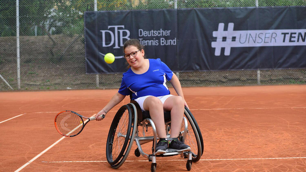 Mädchen beim Tennistraining mit Rollstuhl auf dem Sandplatz