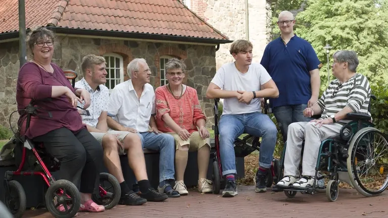 Ein Gruppe von Menschen mit und ohne Behinderung sitzt auf einer Bank