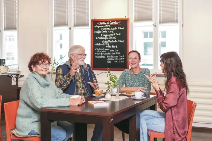 Drei Frauen und ein Mann sitzen am Tisch und reden.