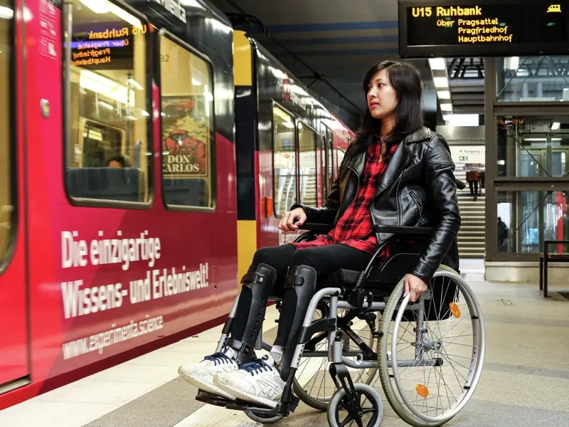 Simone mit ihrem Rollstuhl an einer U-Bahn-Haltestelle. Die Bahn ist gerade eingefahren.
