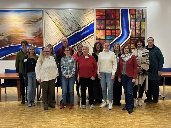 Eine Gruppe von Menschen mit und ohne Behinderung steht zusammen und schaut in die Kamera