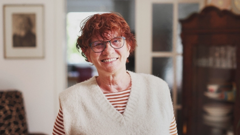 Eine Frau steht in ihrem Wohnzimmer und lächelt.