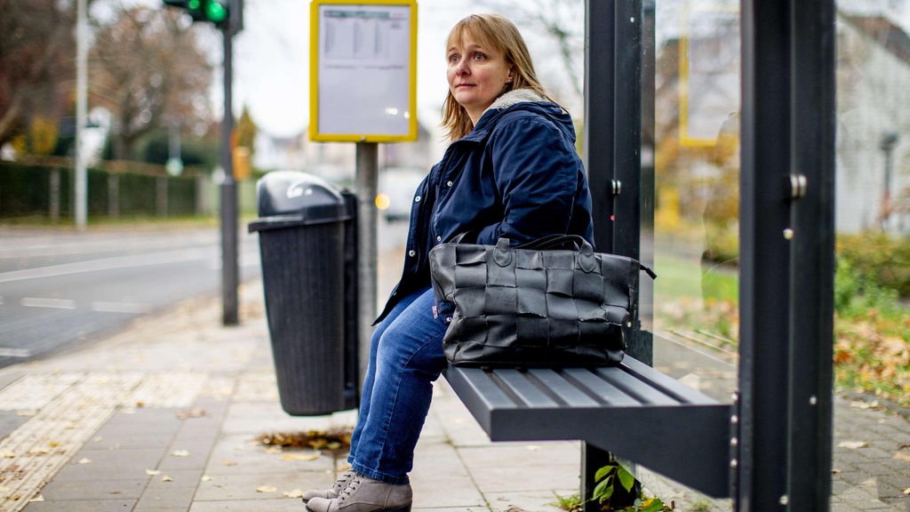Eine Frau sitzt auf einer Bank an einer Bushaltestelle.