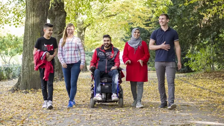 Eine Gruppe von Menschen mit und ohne Behinderung laufen und fahren durch einen Park