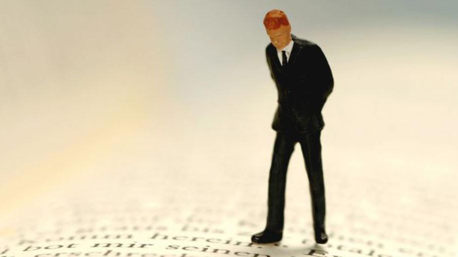 Kleines Figürchen eines Mannes steht auf den Seiten eines Buches und betrachtet die Buchstaben