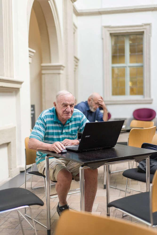 Ein Senior sitzt an einem Laptop in der Bibliothek.