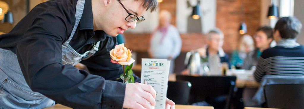 Ein Mann mit Behinderung richtet die Tischdeko in einem Restaurant.