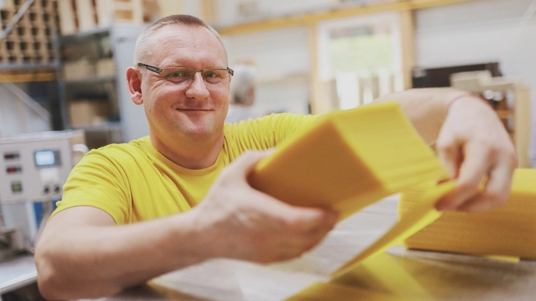 In einem Betrieb für Wachs: Ein Mann hält einen Stapel dünner gelber Wachsplättchen in der Hand und lächelt..