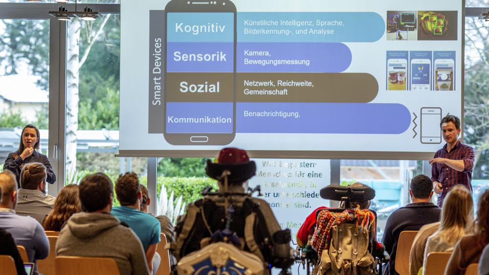 Ein Mann präsentiert einer Gruppe an Menschen eine Powerpoint. Auf der Folie liest man: Digitale Potentiale