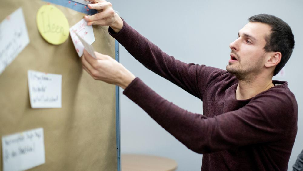 Ein Mann pinnt einen Zettel an eine Pinnwand.