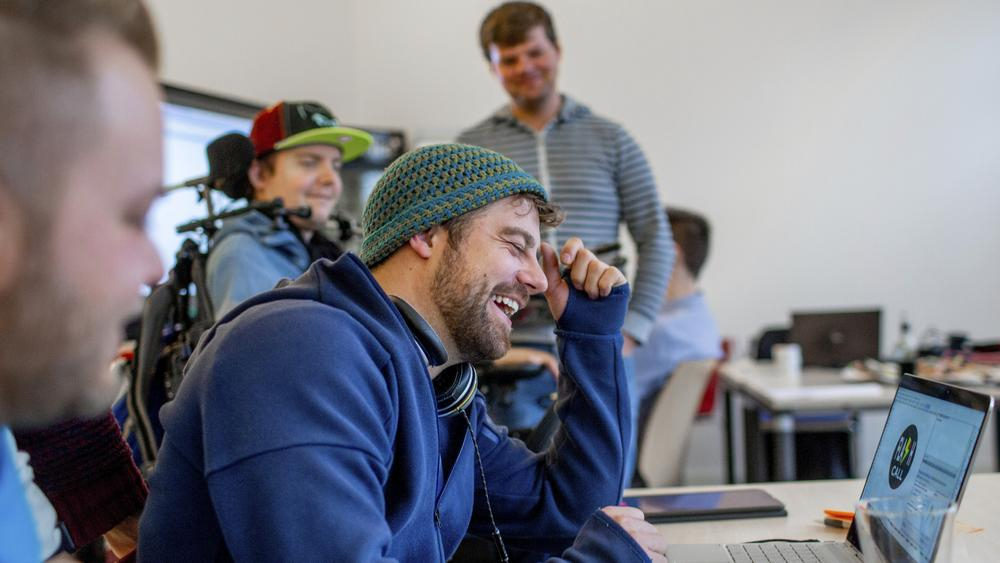 Ein Mann sitzt an einem Laptop und lacht.