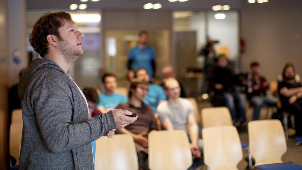 Ein Mann präsentiert einer Menschengruppe seine Idee.