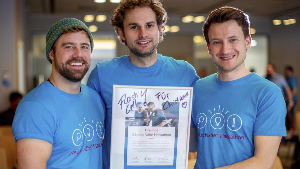 Drei Männer lächeln in die Kamera und halten eine Urkunde.