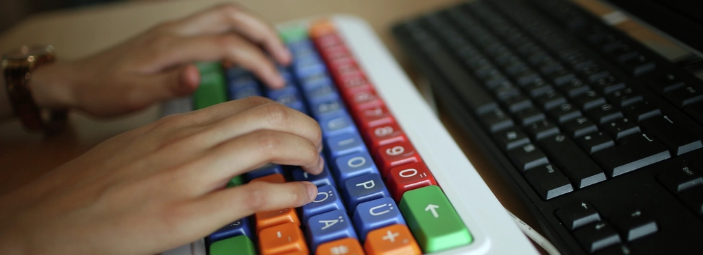 Zwei Hände auf einer bunten Tastatur.