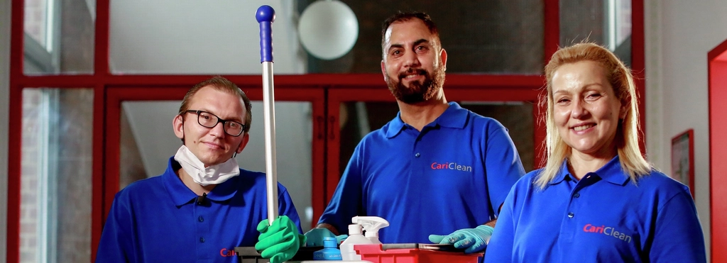 Zwei Männer und eine Frau stehen in Arbeitskleidung neben einem Reinigungswagen und lachen in die Kamera.