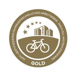 Ein goldener Kreis mit einem Fahrrad und drei Häusern darauf. Um den Kreis herum steht "GOLD. ADFC-zertifizierter fahrradfreundlicher Arbeitgeber. Nach EU-weitem Standard."