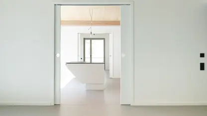 Durch eine breite Schiebetür blickt man in eine Küche mit einer unterfahrbaren Kücheninsel.