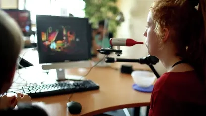 Eine junge Frau sitzt vor einem Bildschirm und nutzt eine Mundmaus.