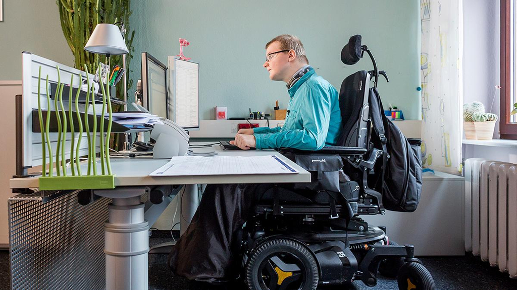 Ein Rollstuhlfahrer arbeitet an einem Computerarbeitsplatz.