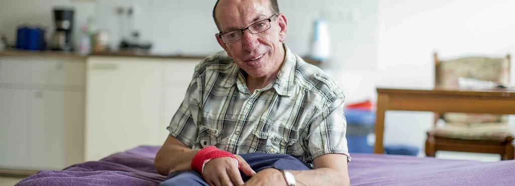 Mann mit geistiger Behinderung sitzt auf seinem Bett in seinem Appartment