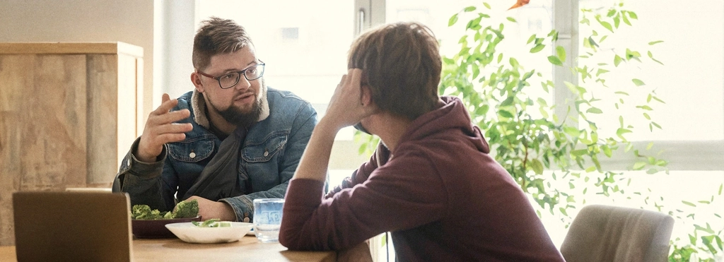 Zwei Menschen sitzen an einem Tisch über Eck und sind in ein Gespräch vertieft.