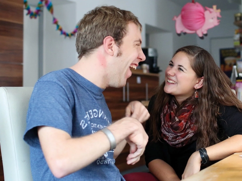 Ein Mann und eine Frau sitzen am Esstisch und lachen gemeinsam.