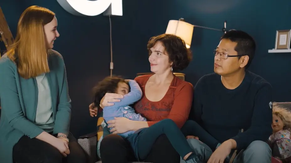 Drei blinde Menschen sitzen nebeneinander und schauen sich ein. In der Mitte sitzt eine Frau, die ein vierjähriges Kind auf dem Schoß hat.