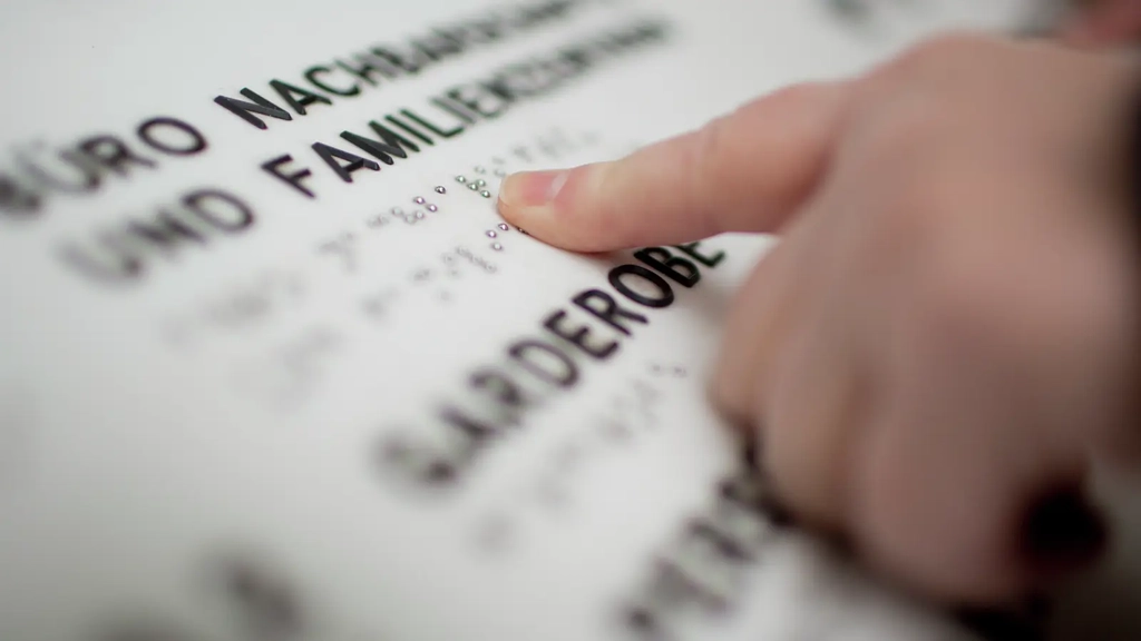 Eine Kinderhand liest einen Text in Brailleschrift.