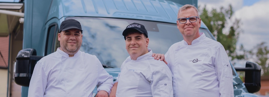 Drei Männer tragen Kochjacken und stehen vor einem Foodtruck.