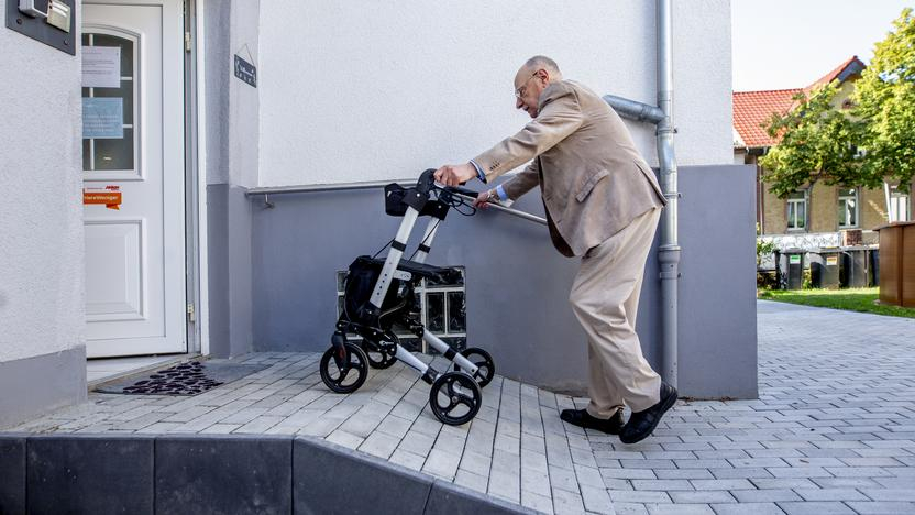 Ein älterer Herr schiebt einen Rollator eine aus Stein gebaute Rampe herauf.