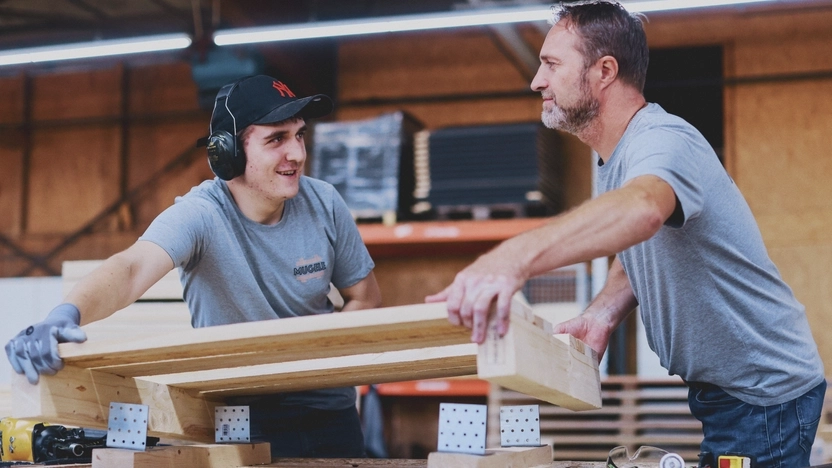 Zwei Männer arbeiten mit Holz in einer Werkstatt.