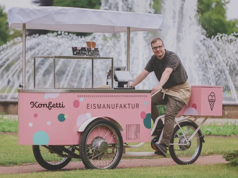 Ein Mann sitzt auf dem Sattel eines Eismobils. Das Mobil ist rosafarben und hat einen weißen Baldachin.