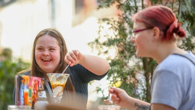 Zwei junge Frauen essen auf einem Balkon gemeinsam Eis.