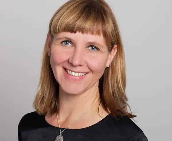Porträt einer Frau mit schulterlangem blonden Haar und kurzem Pony. Sie lächelt in die Kamera.