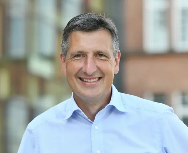 Porträt eines Mannes mit kurzem grauen Haar. Er trägt ein kurzärmeliges Hemd und lächelt in die Kamera.