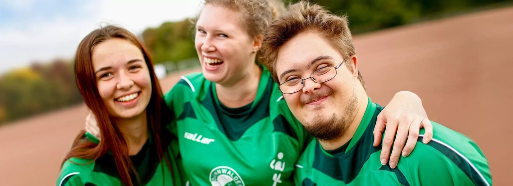 Drei Jugendliche in Sporttrikot umarmen sich.