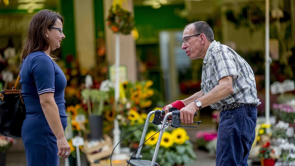 Mann mit Rollator und eine Frau unterhalten sich auf der Straße vor einem Blumenladen