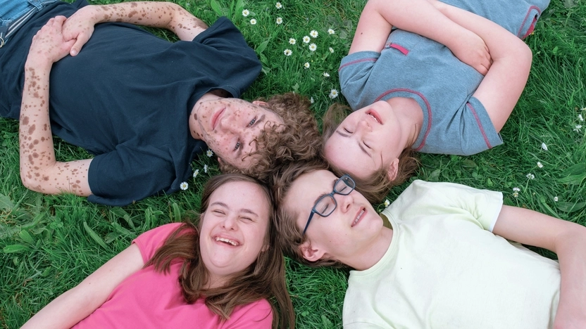 Vier Jugendliche liegen Kopf an Kopf auf einer Wiese.