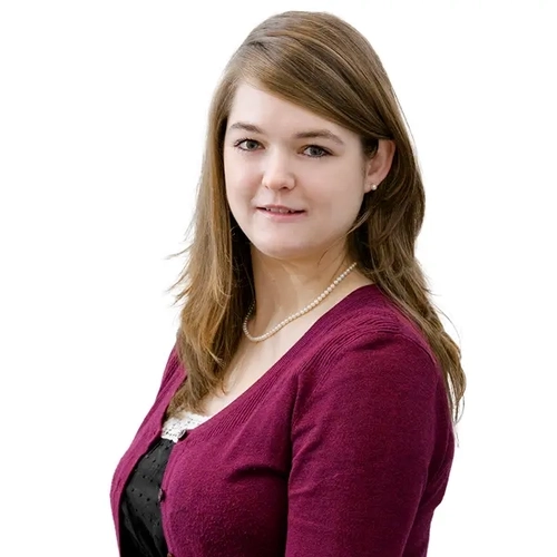 Porträt einer jungen Frau mit langem braunen Haar. Sie trägt eine weinrote Strickjacke und schaut direkt in die Kamera.