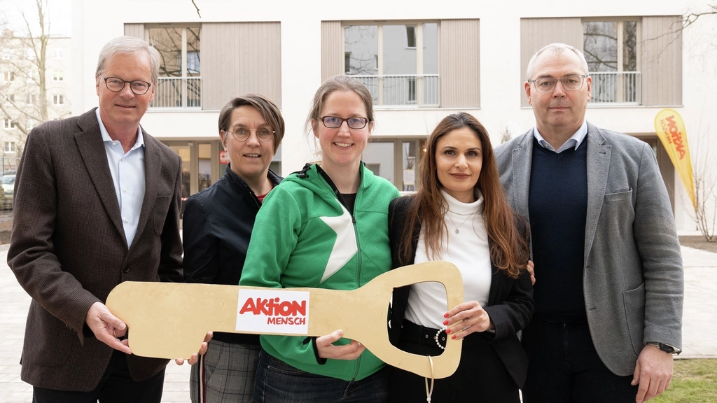 Vertreter*innen der Aktion Mensch, der Stephanus-Stiftung und neue Bewohnerinnen des inklusiven Wohnprojekts der Aktion Mensch steht vor dem Haus in Berlin und halten alle gemeinsam einen großen goldenen Schlüssel in der Hand, auf dem das Aktion Mensch Logo zu sehen ist.