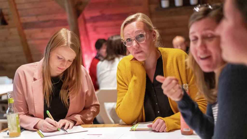 Mehrere Frauen sitzen an einem Tisch und arbeiten gemeinsam an einem Projekt